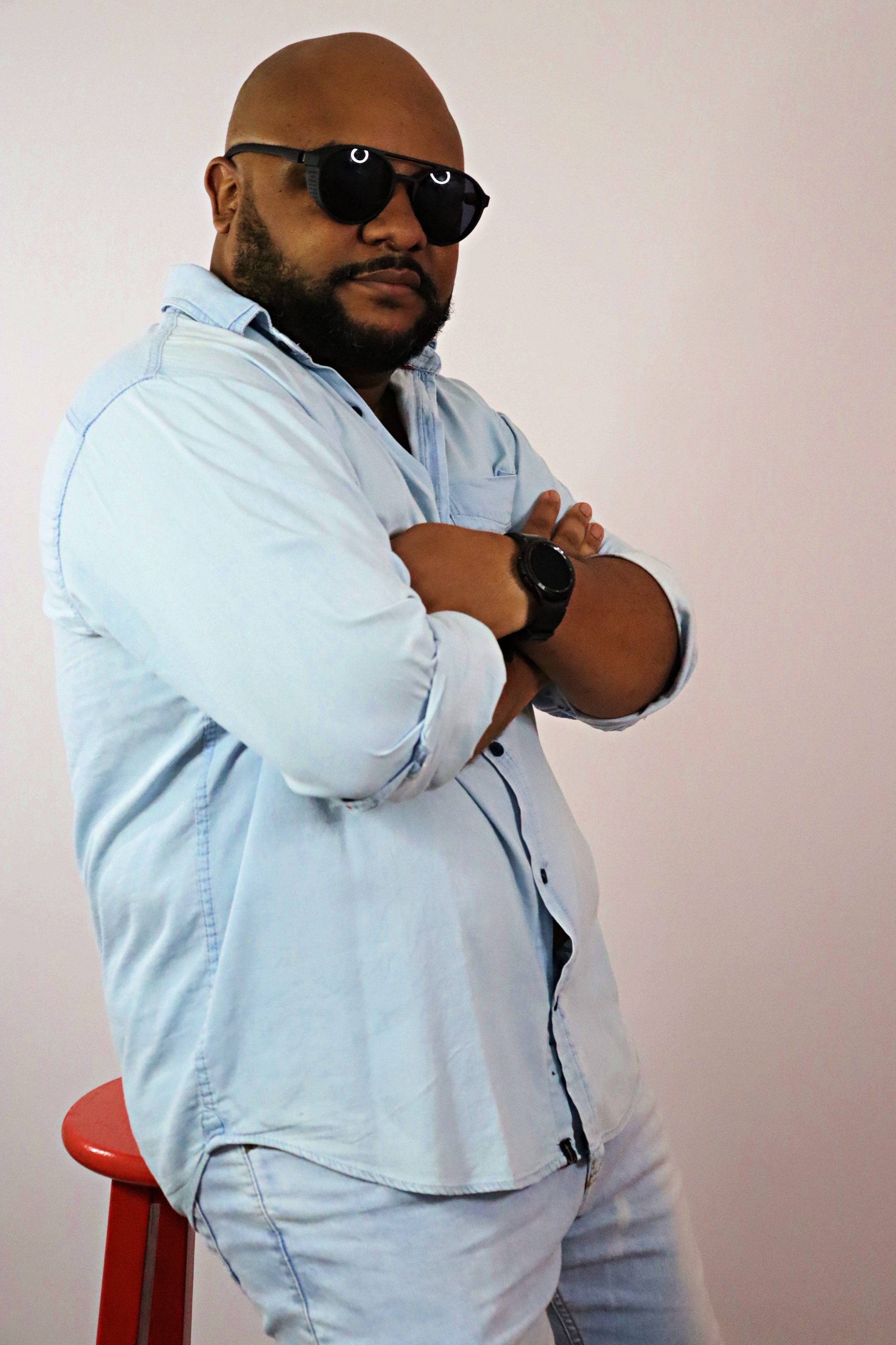 Xandão de camisa jeans clara, óculos escuros e braços cruzados